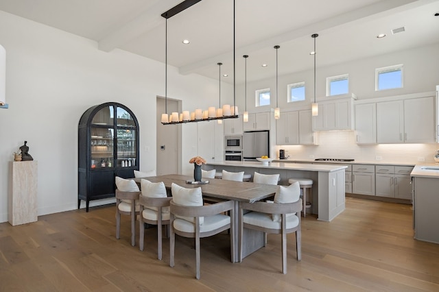 dining room with beamed ceiling, a towering ceiling, and light wood-type flooring