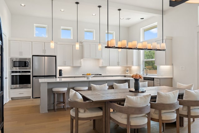 kitchen with white cabinetry, stainless steel appliances, decorative light fixtures, and a center island