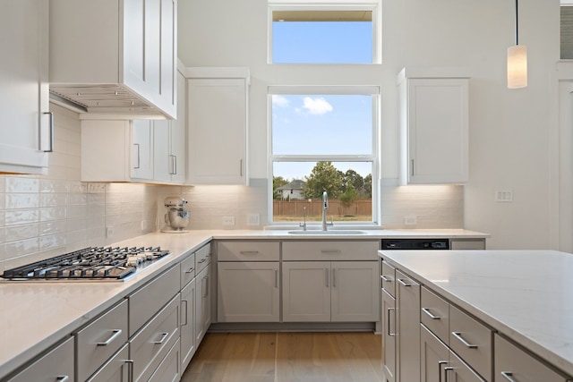 kitchen with light stone countertops, backsplash, light wood-type flooring, sink, and pendant lighting