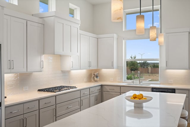 kitchen with sink, gray cabinetry, light stone counters, pendant lighting, and stainless steel gas stovetop