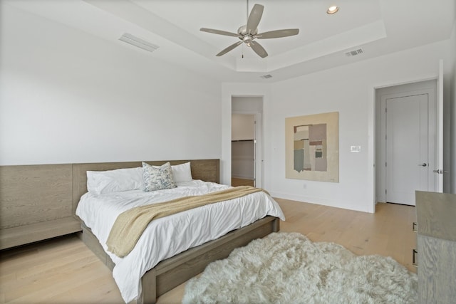 bedroom with a tray ceiling, ceiling fan, and light wood-type flooring