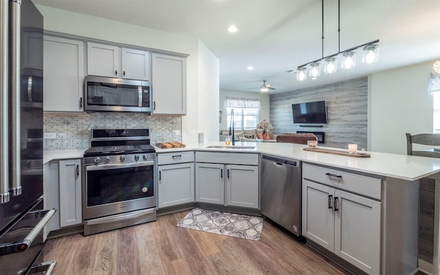 kitchen with dark wood-type flooring, gray cabinets, appliances with stainless steel finishes, decorative light fixtures, and kitchen peninsula