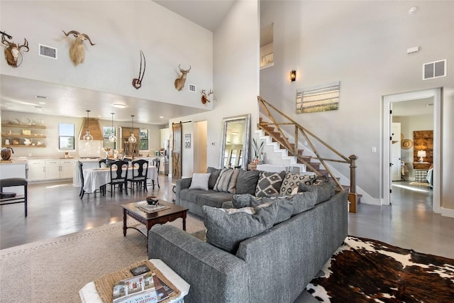 living room featuring visible vents, a high ceiling, and stairs