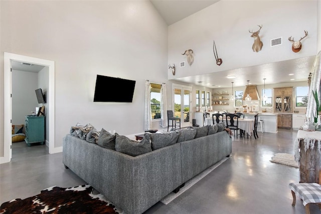 living area with concrete flooring, a towering ceiling, visible vents, and baseboards