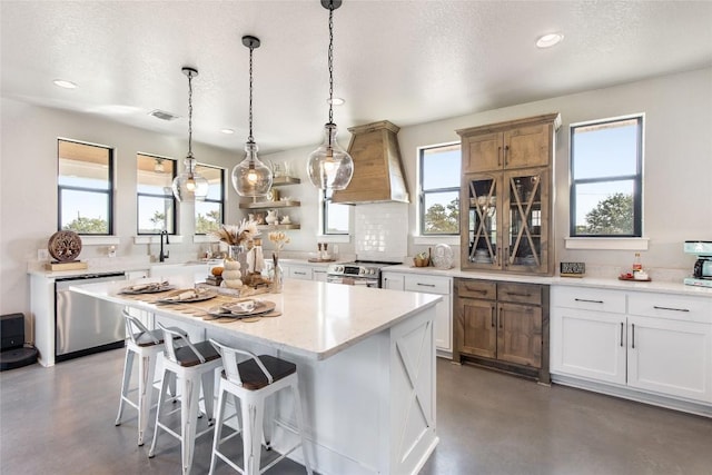 kitchen with concrete flooring, a wealth of natural light, appliances with stainless steel finishes, and custom exhaust hood