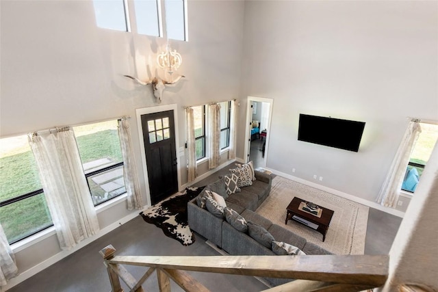living area featuring a high ceiling, baseboards, a notable chandelier, and a healthy amount of sunlight
