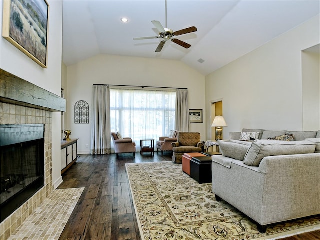 living room with dark wood-style flooring, a ceiling fan, vaulted ceiling, a tile fireplace, and baseboards