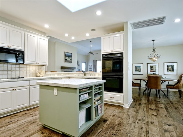 kitchen with tile countertops, wood finished floors, visible vents, white cabinetry, and black appliances