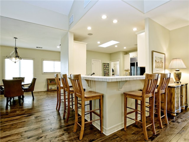 kitchen featuring visible vents, tile counters, white cabinets, a breakfast bar area, and dark wood-style flooring