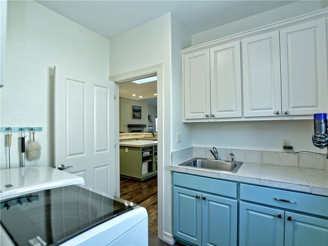 kitchen with blue cabinets, dark wood-type flooring, a sink, white cabinetry, and light countertops