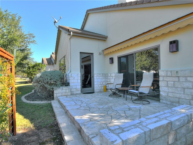 rear view of house with stone siding, a patio, and stucco siding