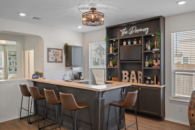 bar featuring sink, light wood-type flooring, a wealth of natural light, and decorative backsplash