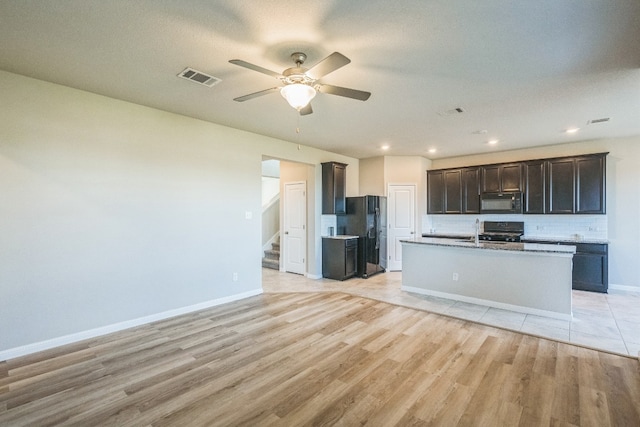 kitchen with ceiling fan, light hardwood / wood-style flooring, an island with sink, and black appliances