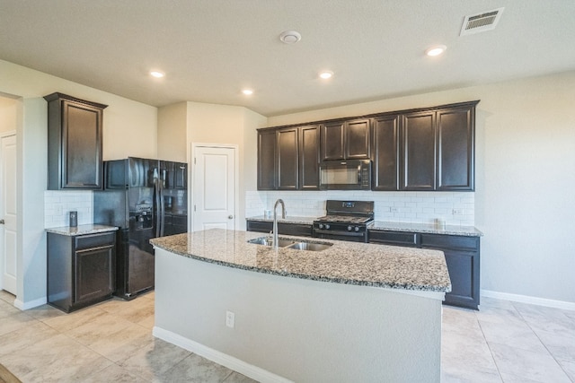 kitchen featuring decorative backsplash, light stone countertops, sink, black appliances, and a center island with sink