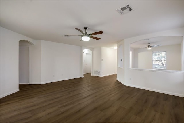 empty room featuring arched walkways, dark wood finished floors, visible vents, ceiling fan, and baseboards