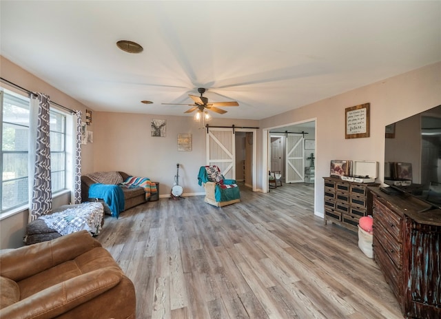 living room featuring a barn door, light hardwood / wood-style floors, and ceiling fan