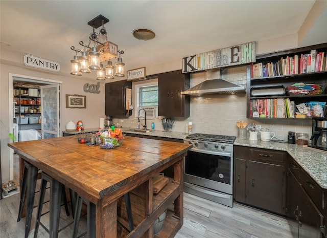 kitchen featuring wall chimney range hood, decorative light fixtures, light wood-type flooring, dark brown cabinets, and gas stove