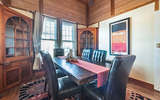 dining space featuring wooden walls, hardwood / wood-style floors, and vaulted ceiling