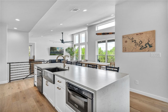 kitchen featuring white cabinetry, ceiling fan, sink, a center island with sink, and light wood-type flooring