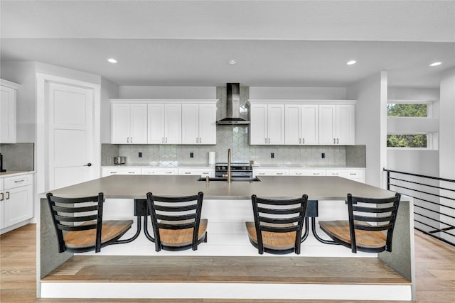 kitchen featuring a kitchen bar, an island with sink, and wall chimney range hood