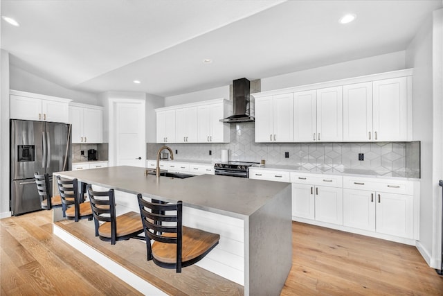 kitchen featuring appliances with stainless steel finishes, light wood-type flooring, wall chimney exhaust hood, a kitchen island with sink, and sink