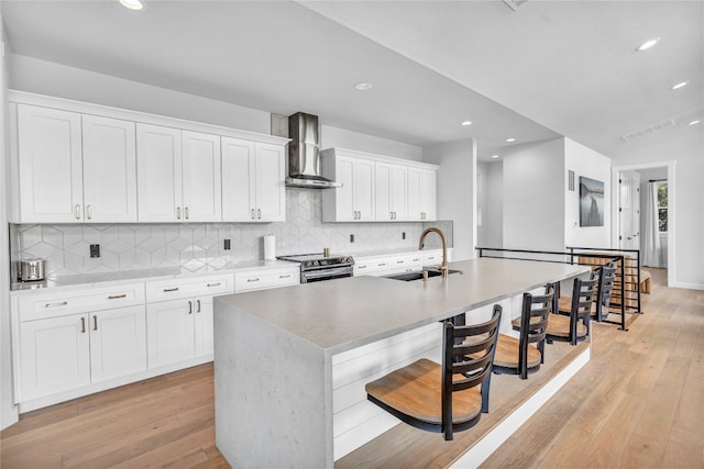 kitchen featuring wall chimney exhaust hood, a kitchen island with sink, sink, light hardwood / wood-style floors, and white cabinetry