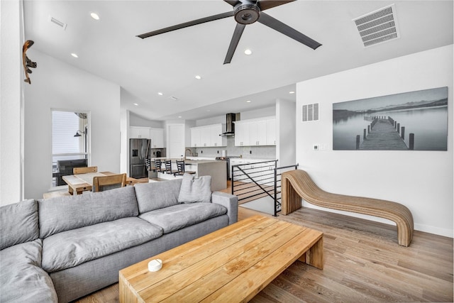 living room with ceiling fan, light hardwood / wood-style floors, sink, and vaulted ceiling