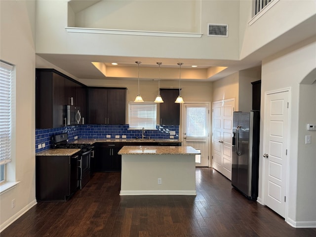 kitchen featuring a center island, dark wood-type flooring, a high ceiling, stainless steel appliances, and decorative light fixtures