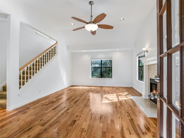 unfurnished living room featuring ceiling fan, light hardwood / wood-style flooring, a tile fireplace, and vaulted ceiling