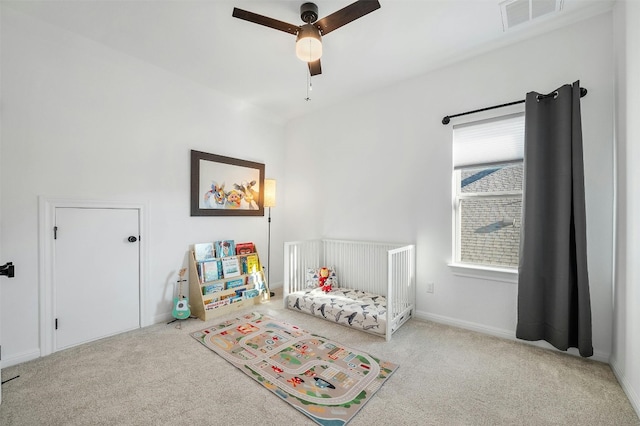 carpeted bedroom featuring ceiling fan and a nursery area