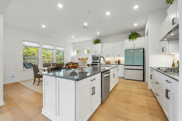 kitchen with a kitchen island with sink, white cabinets, stainless steel appliances, and light wood-type flooring