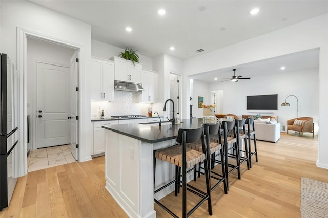 kitchen with white cabinets, an island with sink, and light wood-type flooring