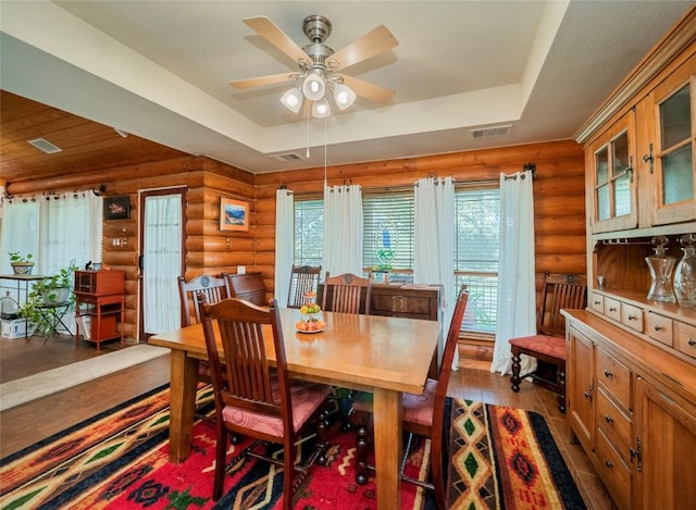 dining space featuring hardwood / wood-style flooring, ceiling fan, a tray ceiling, and rustic walls