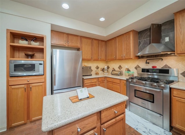 kitchen with wall chimney range hood, stainless steel appliances, a center island, tasteful backsplash, and light stone counters