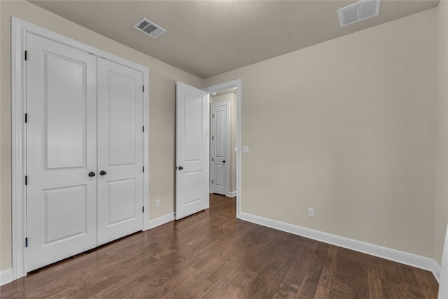 unfurnished bedroom with a textured ceiling, a closet, and dark hardwood / wood-style floors