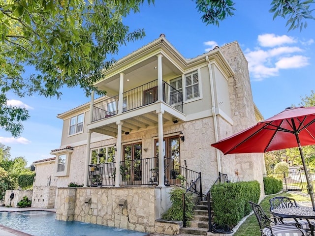 back of property featuring pool water feature, a balcony, a fenced in pool, and french doors