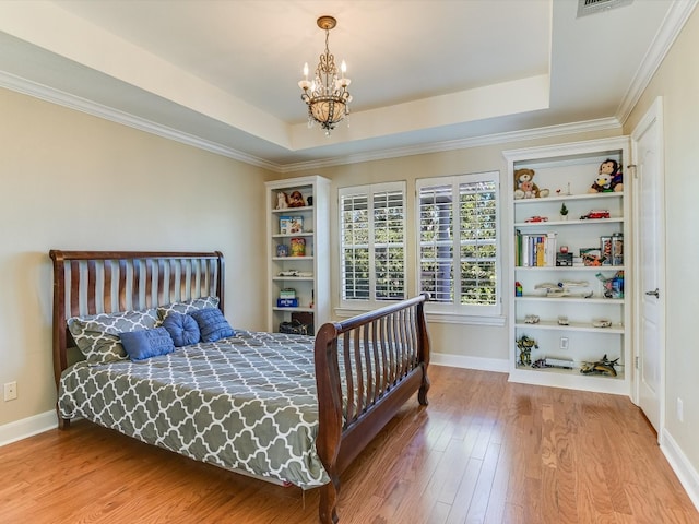 bedroom with wood-type flooring, ornamental molding, a tray ceiling, and a chandelier