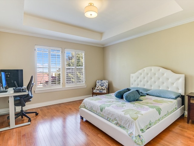 bedroom with ornamental molding, hardwood / wood-style flooring, and a tray ceiling