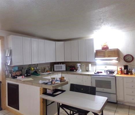 kitchen featuring a kitchen bar, a textured ceiling, white appliances, white cabinetry, and light tile patterned flooring