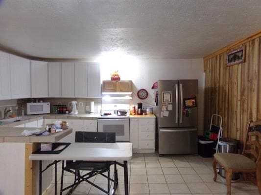 kitchen featuring white cabinetry, kitchen peninsula, white appliances, a breakfast bar area, and light tile patterned flooring