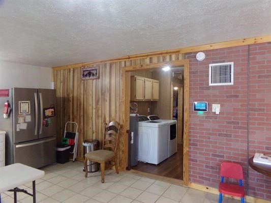 kitchen with wood walls, a textured ceiling, stainless steel refrigerator, light tile patterned flooring, and washer / clothes dryer