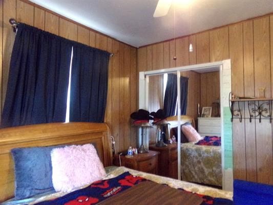 bedroom featuring ceiling fan and wood walls