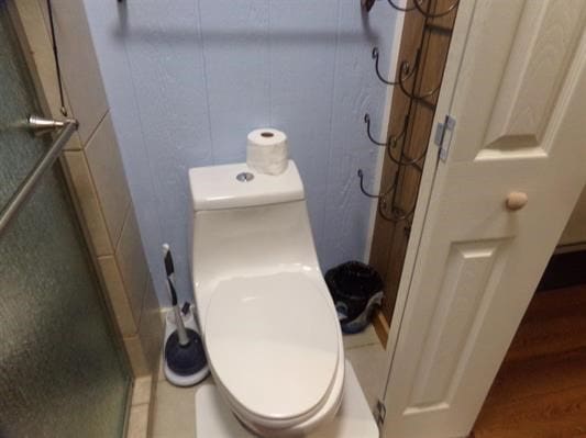 bathroom with hardwood / wood-style flooring, a shower with shower door, and toilet