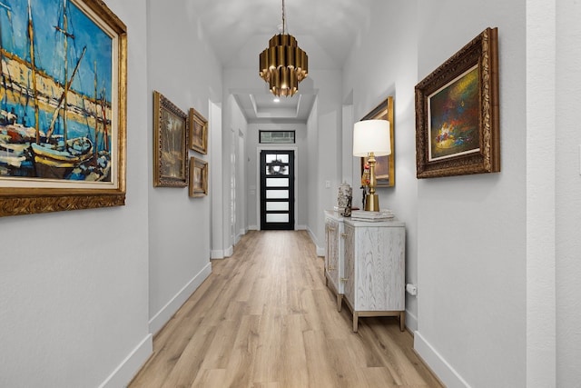 corridor with a raised ceiling, light hardwood / wood-style floors, and a notable chandelier