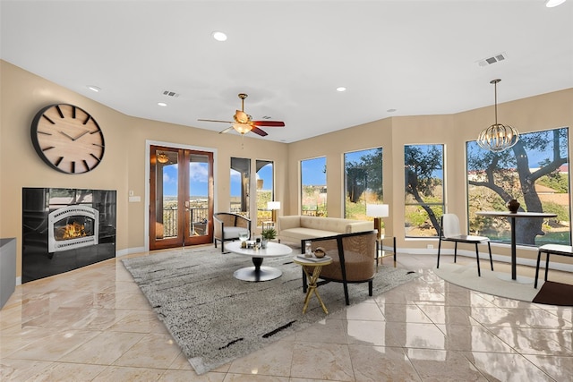 living room with plenty of natural light, a fireplace, ceiling fan with notable chandelier, and french doors