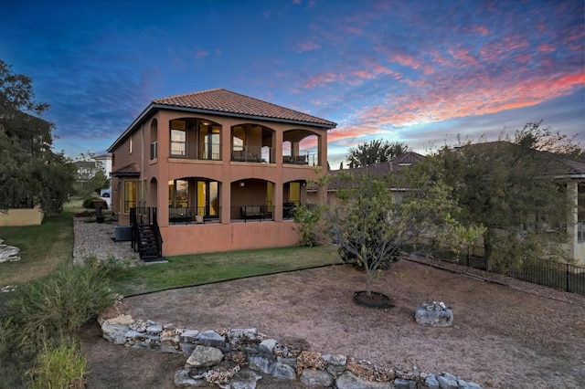 back house at dusk featuring central air condition unit, a balcony, and a lawn