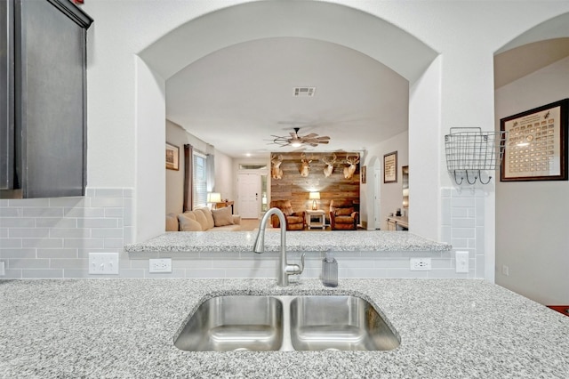 kitchen featuring tasteful backsplash, light stone countertops, sink, and ceiling fan