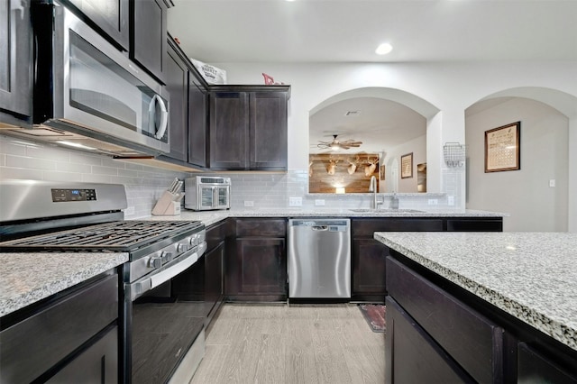 kitchen featuring sink, decorative backsplash, light wood-type flooring, light stone counters, and stainless steel appliances