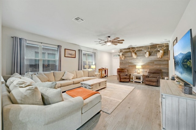 living room with light hardwood / wood-style floors, ceiling fan, and wood walls