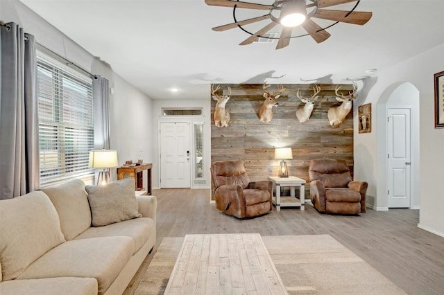 living room with ceiling fan, wooden walls, and light hardwood / wood-style floors